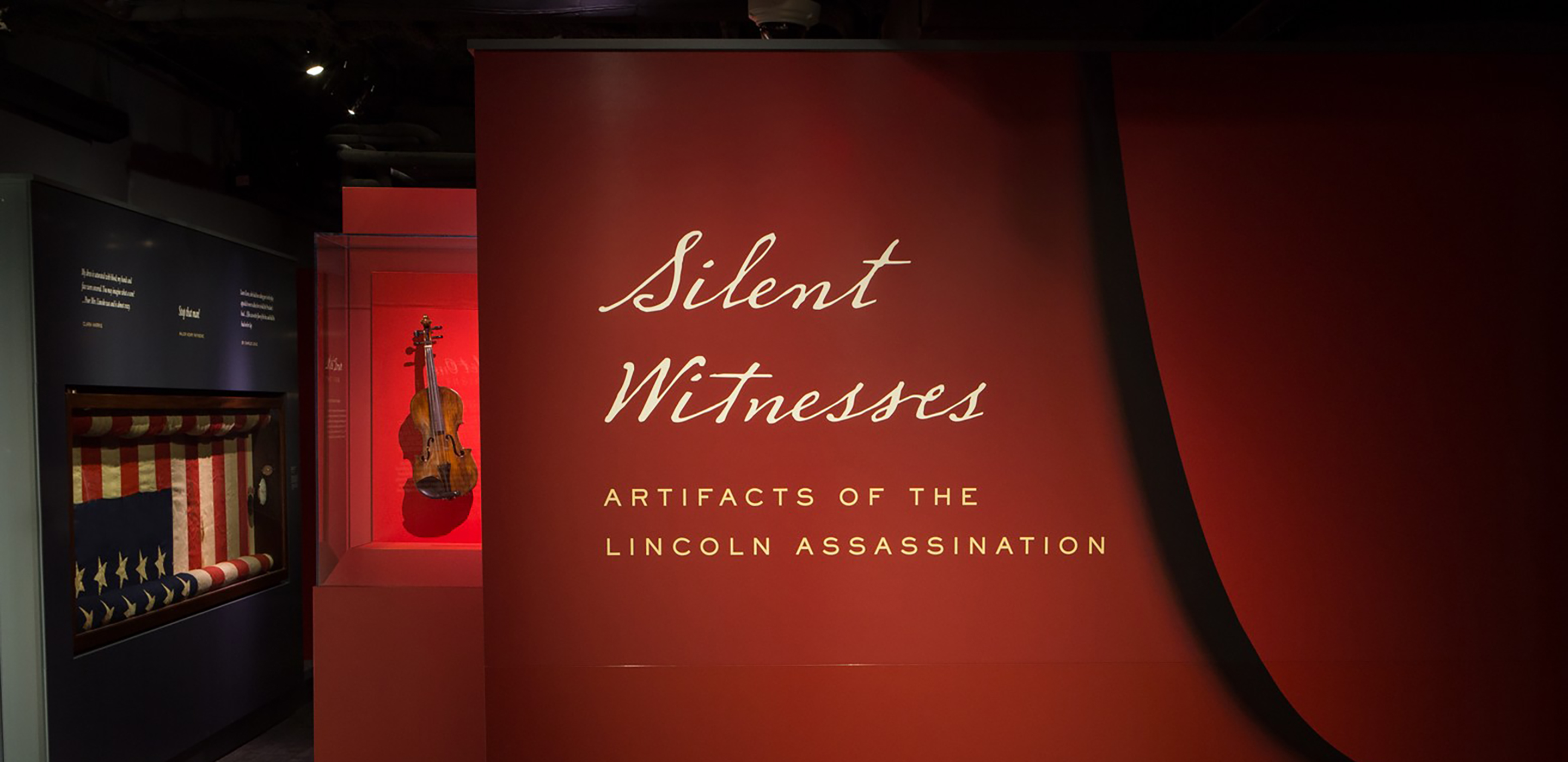 Entry view of the red paneled walls and museum cases for the 2015 “Silent Witnesses” exhibition at the Center for Education and Leadership. Artifact shown is a violin and bow played in the orchestra at Ford's the night of the assassination.