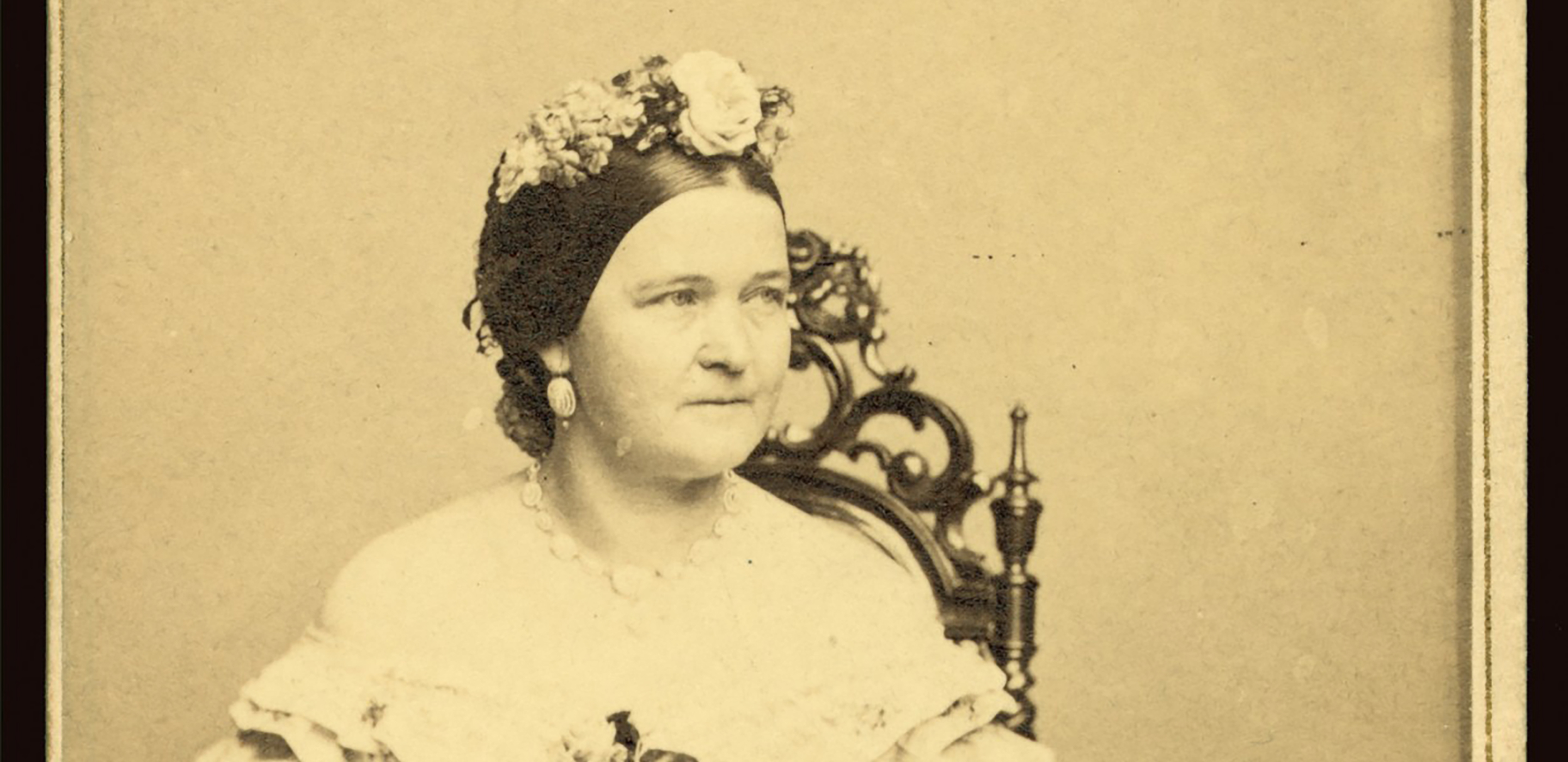 Sepia photograph of Mary Todd Lincoln seated in a chair, wearing a floral headdress and a white dress.