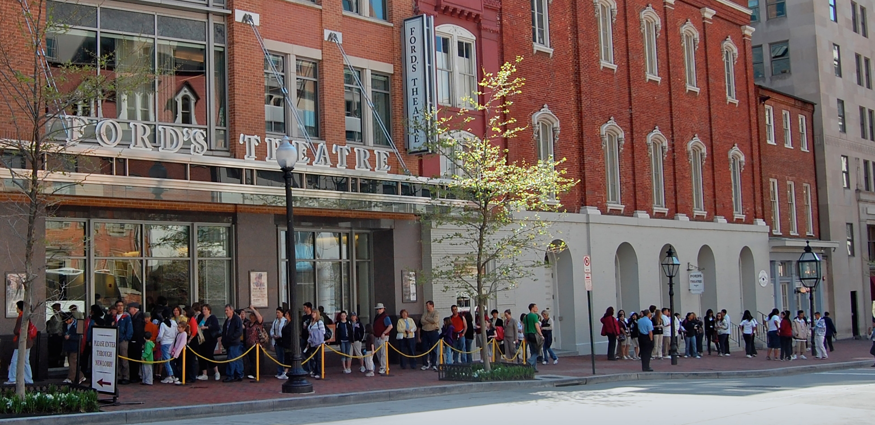 Daytime visitors stand in line on Tenth Street, waiting to enter the lobby of Ford’s Theatre to start their tour or the site.