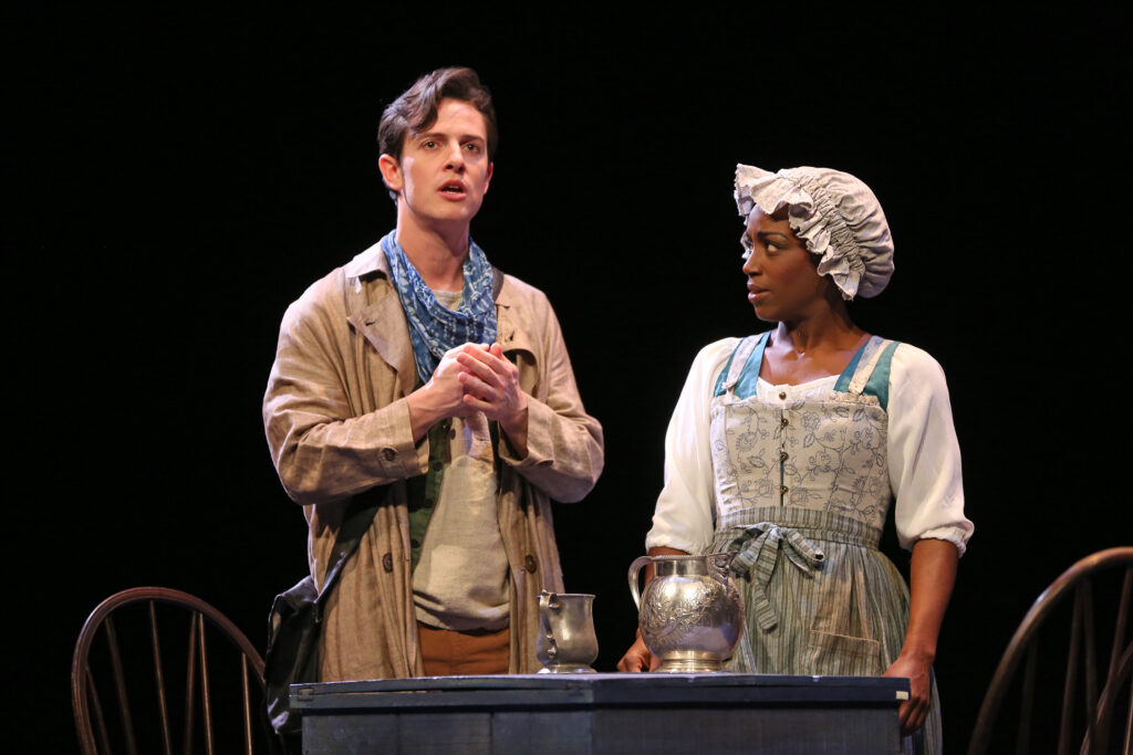A young free man stands and gives an impassioned speech. A young enslaved woman looks at him with disbelief. Both wear 18th-century clothes.