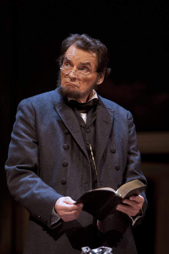 An actor portraying Abraham Lincoln stands and looks right while holding a bible.