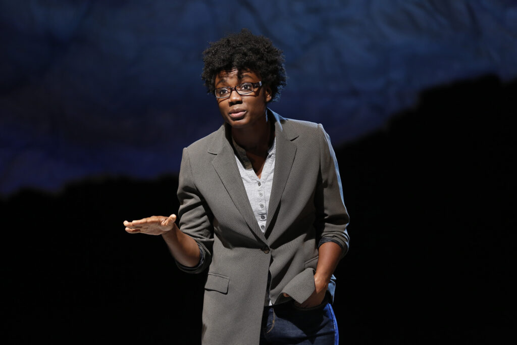 A woman in a suit jacked and wearing glasses gestures with her hand while speaking to the audience.