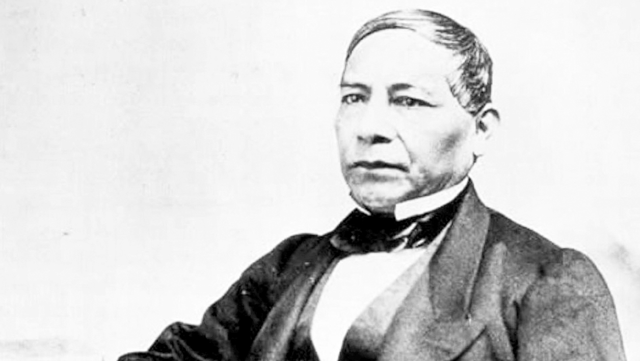 Black and white photograph of a seated Latino man wearing a suit.