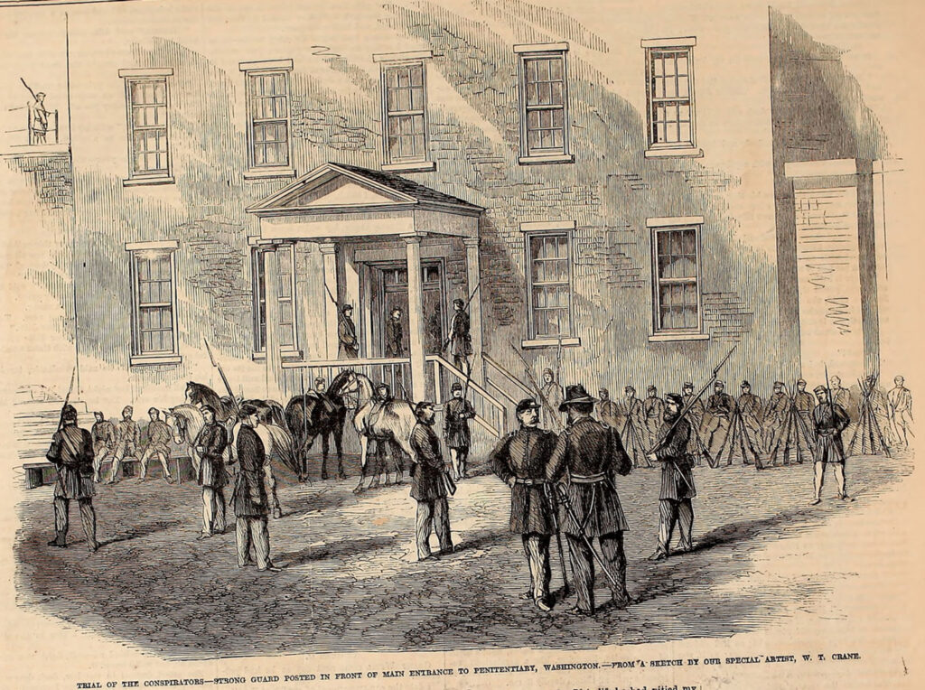 A drawing of a group of soldier guarding a large brick building. A caption reads" Trial of the conspirators - Strong guard posted in front of main entrance to penitentiary, Washington - From a sketch by our special artist, W. T. Crane.