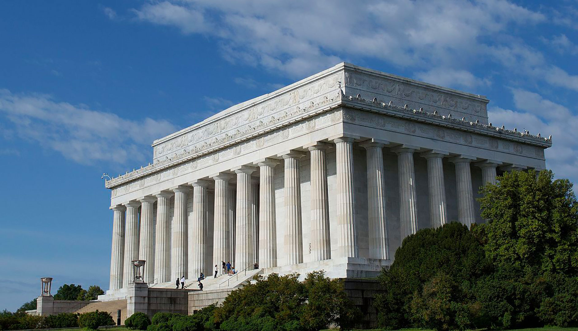 Daytime view of an enormous, temple-like marble structure lined with white columns.