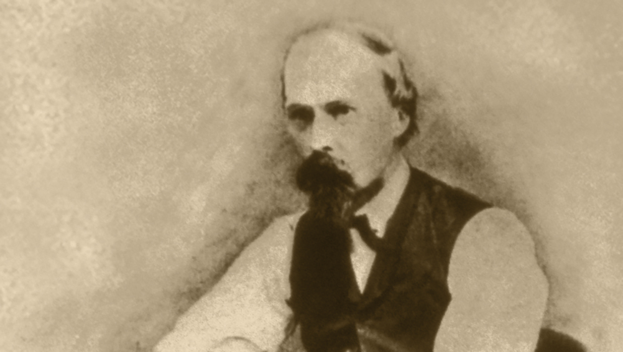 A blurry sepia photograph of a man with a mustache and beard wearing a jacketless suit.