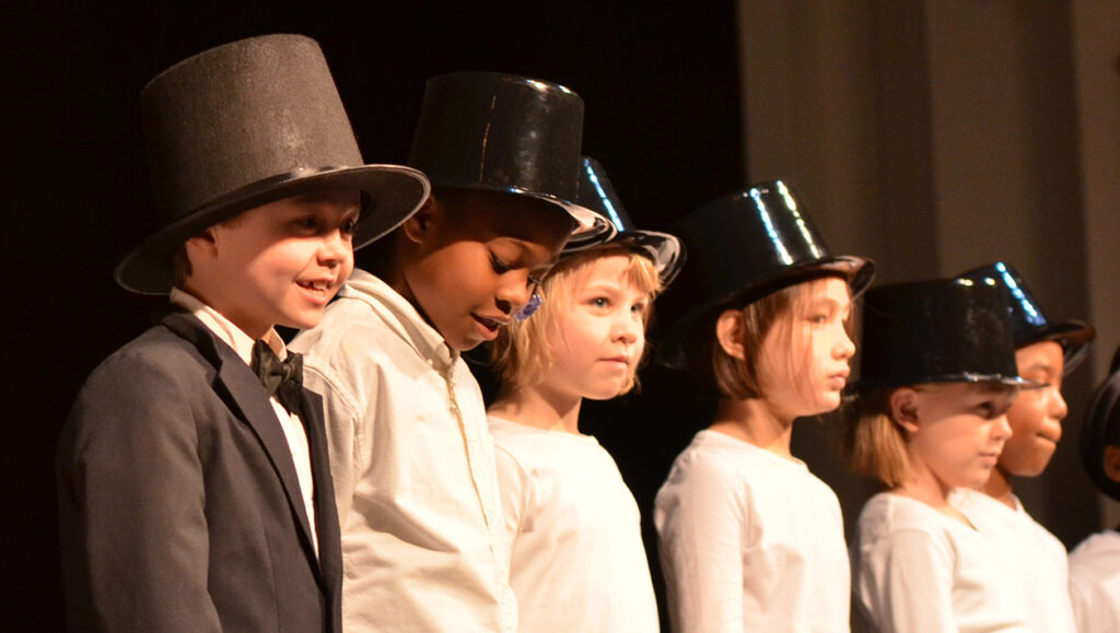 A row of children stand on the Ford's Theatre stage dressed in white shirts and stovepipe hats.